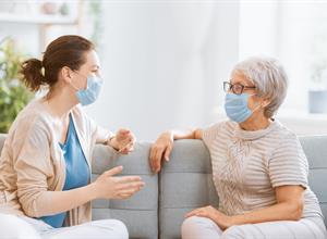  Caregiver And Senior talking in a living facility wearing ppe